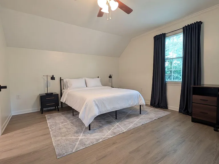 Spacious bedroom with a ceiling fan, large window with curtain panels, and room for a full furniture setup.