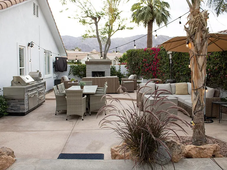 View of the outdoor living space. Gas fireplace with couch, two lounge chairs and coffee table. Dining area. Sectional area with a firepit. All with views of the golf course.