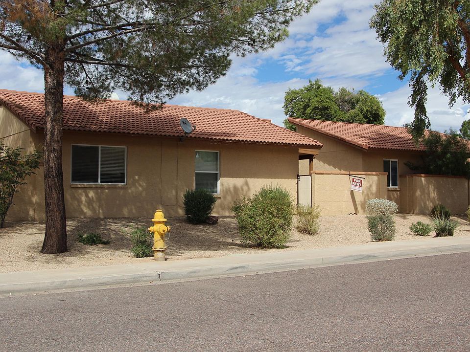 Rear exterior of home. Master bedroom window on left, living room window to the right. Patio area (with the For Rent sign) to the far right has a secured gate to the street/home.