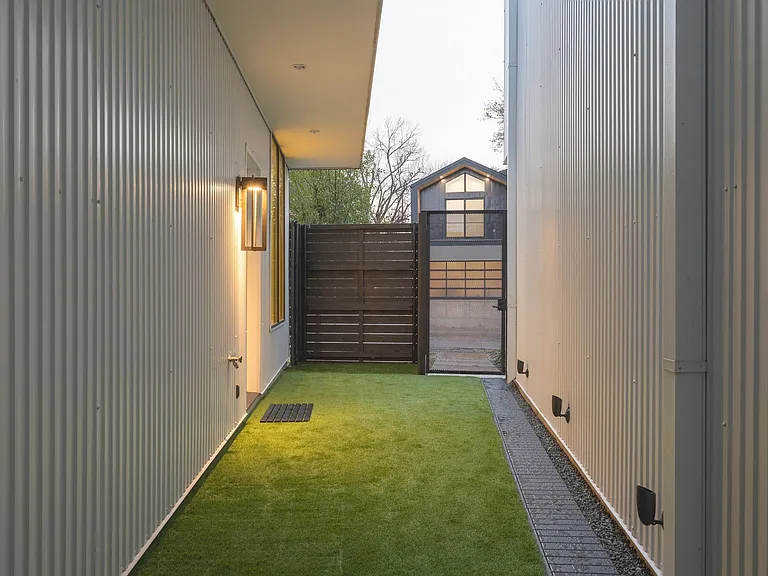 Covered outdoor walkway featuring corrugated metal siding, recessed lighting, and a modern wall sconce