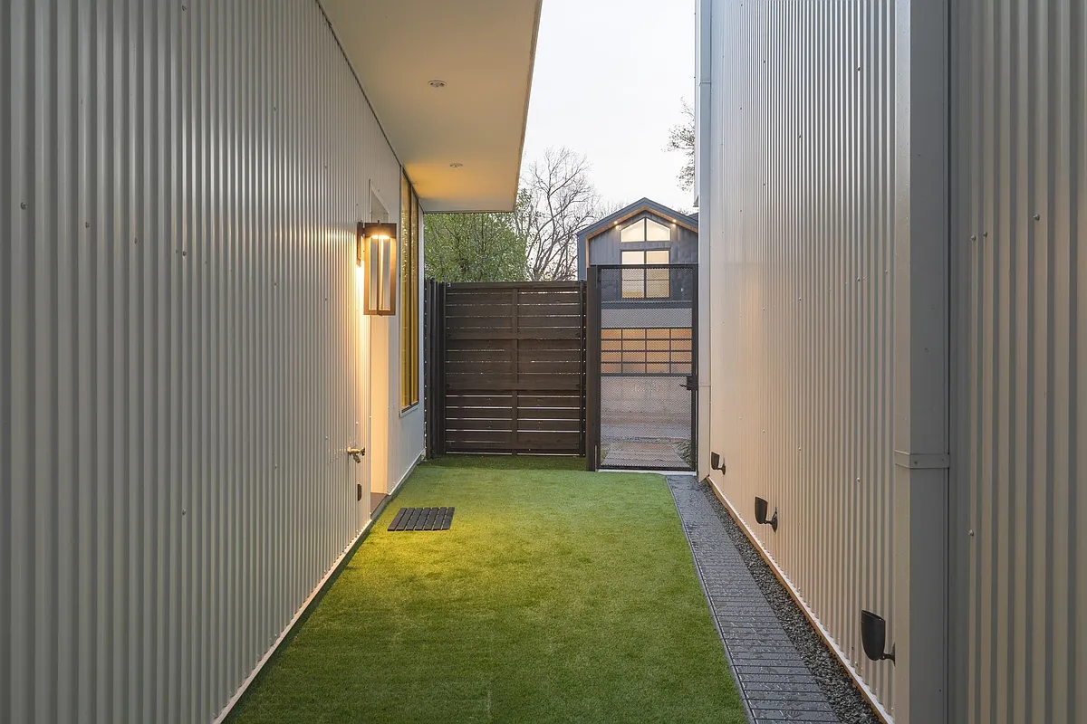 Covered outdoor walkway featuring corrugated metal siding, recessed lighting, and a modern wall sconce - 2422 N Carroll Ave #2