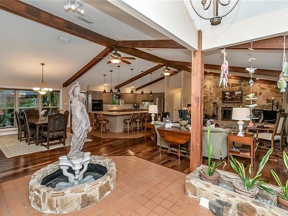 Living area featuring wood finished floors, visible vents, vaulted ceiling with beams, and ceiling fan with notable chandelier