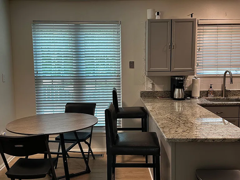 Eat-in kitchen area with granite counters, bar seating, and a small dining table set beside large windows with blinds.