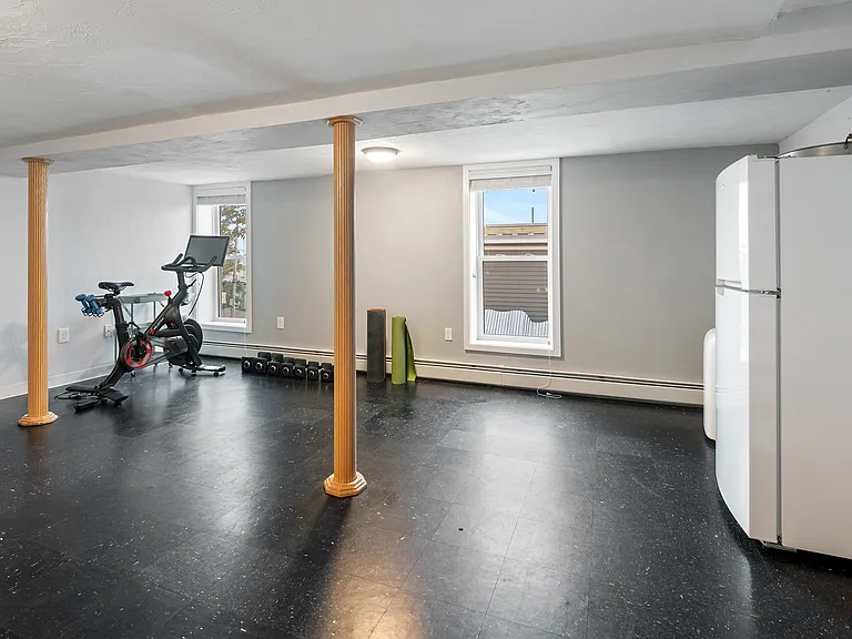 Small basement gym space with stationary bike, hand weights, and yoga mats