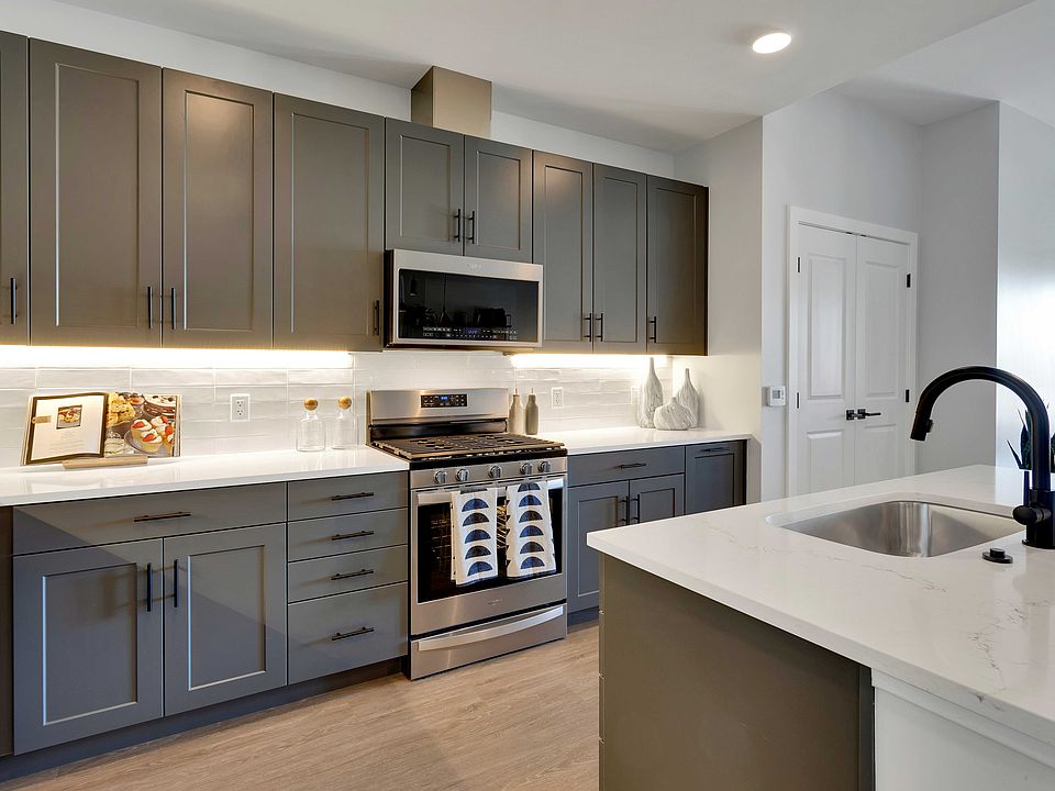 Modern kitchen with sleek grey cabinets, stainless steel appliances, and elegant white countertops, featuring a stylish island sink.
