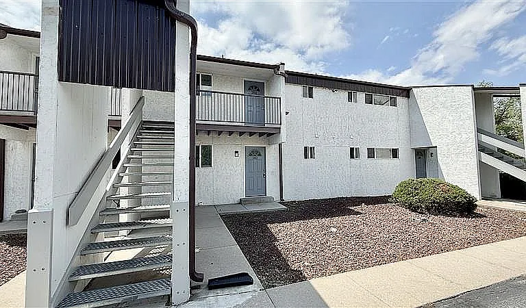 Charming apartment exterior with contemporary design, featuring white walls, stylish gray doors, and outdoor stairway access.