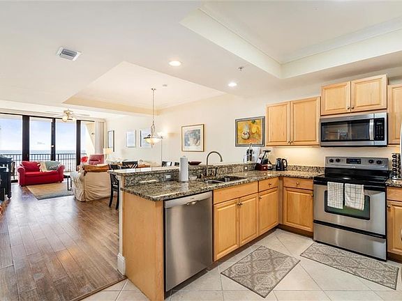 Kitchen with light hardwood / wood-style floors, a raised ceiling, dark stone counters, sink, and stainless steel appliances