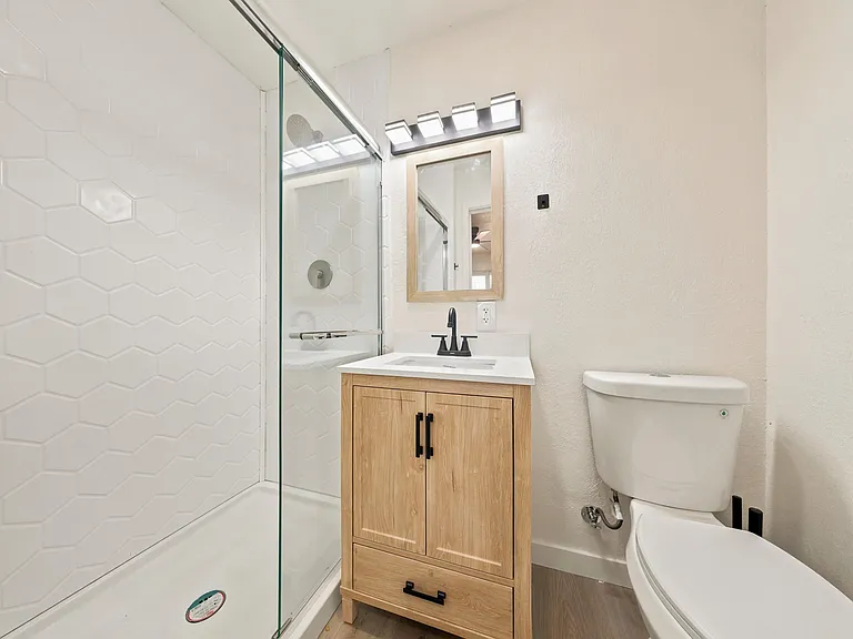 Full bath with a glass-enclosed tub/shower, hex-tile surround, and a vanity with storage and updated lighting.