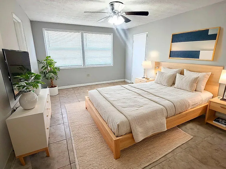Bright and inviting bedroom with a modern design, featuring a cozy wooden bed, contemporary artwork, and serene natural lighting.