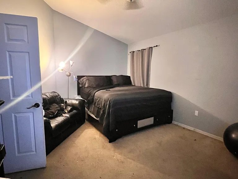 Spacious bedroom with a large bed, neutral walls, carpet flooring, and a window with curtains for privacy.