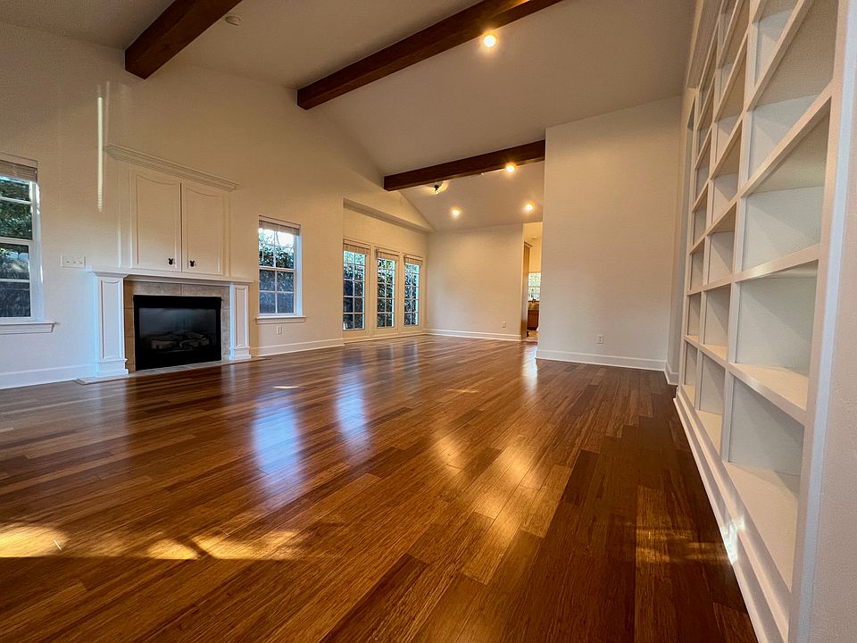 In the living room and dining room area there are hardwood floors, vaulted ceilings, exposed beams, a gas log fireplace, and walls of bookshelves.