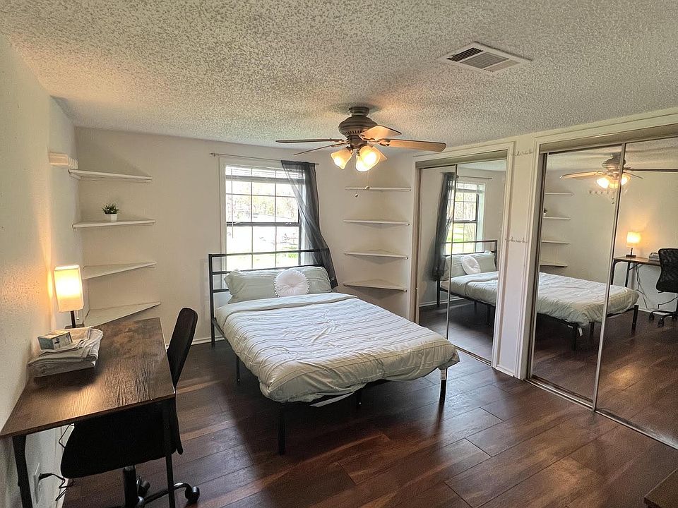 Furnished bedroom with hardwood floors, ceiling fan, built-in wall shelving, and a mirrored closet for added storage.