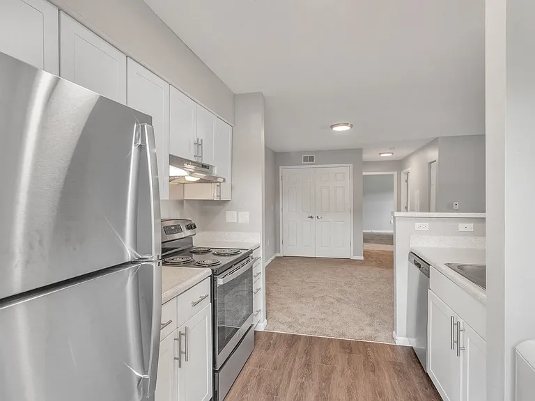 Open-concept living with hardwood kitchen floors flowing into the carpeted living room, stainless steel appliances, and abundant natural light, professionally managed by Highlands Vista Group.