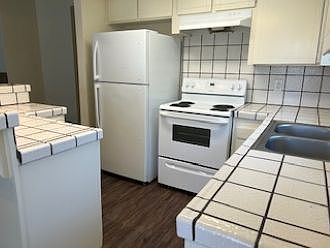 Light & bright kitchen with refrigerator, stove and hood, dual stainless steel sink with pot-style faucet, and dishwasher
