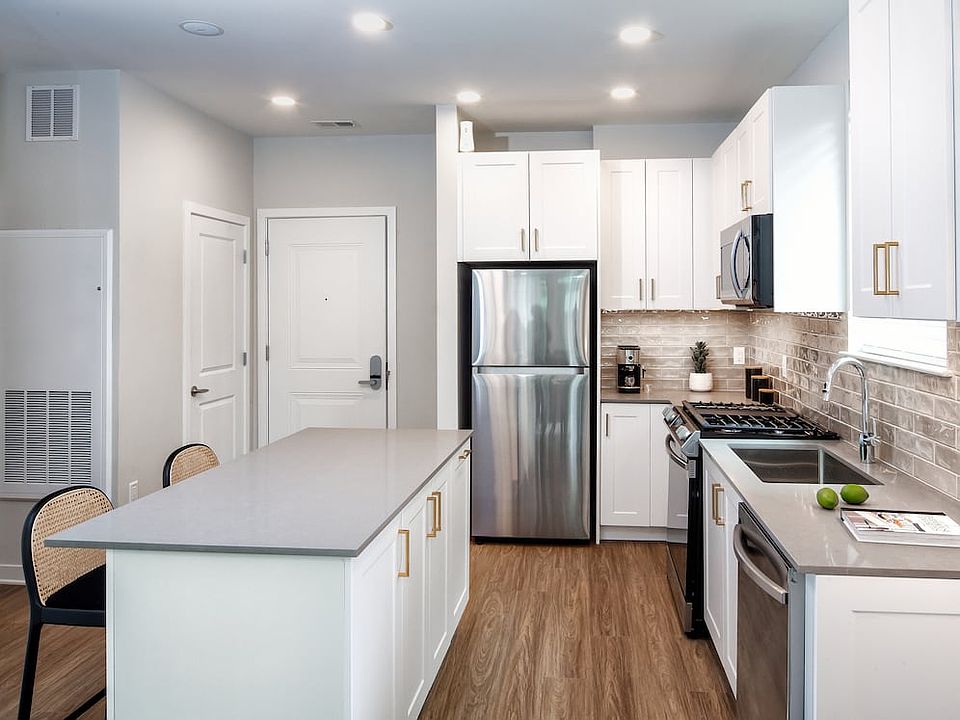 Design Collection II (South Building) Kitchen with white cabinetry, gold pulls, beige tile backsplash, grey quartz countertops, stainless steel appliances, and hard surface flooring