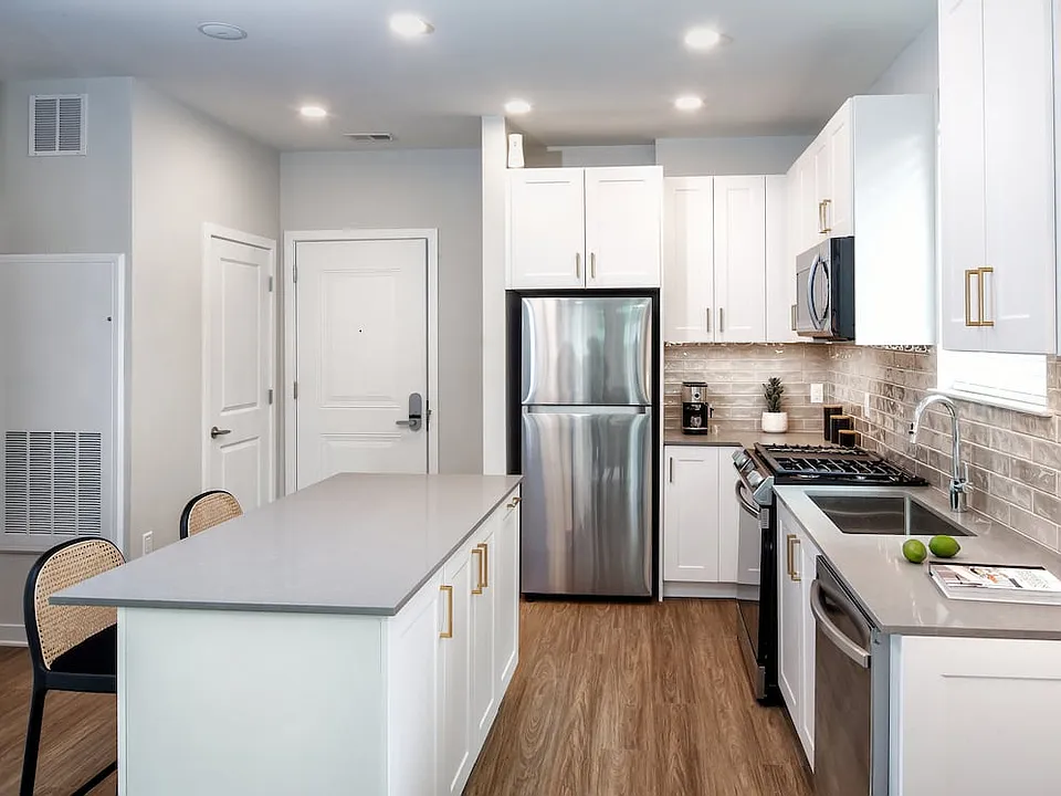 Design Collection II (South Building) Kitchen with white cabinetry, gold pulls, beige tile backsplash, grey quartz countertops, stainless steel appliances, and hard surface flooring