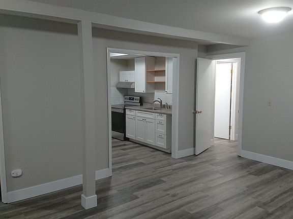 Main living space with view into bedroom (left), open kitchen, hall to garage with bath (right)