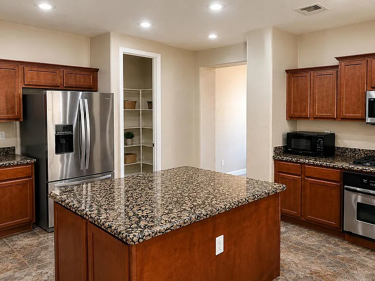 Spacious kitchen with a large granite island, stainless steel appliances, ample cabinetry, and a walk-in pantry.