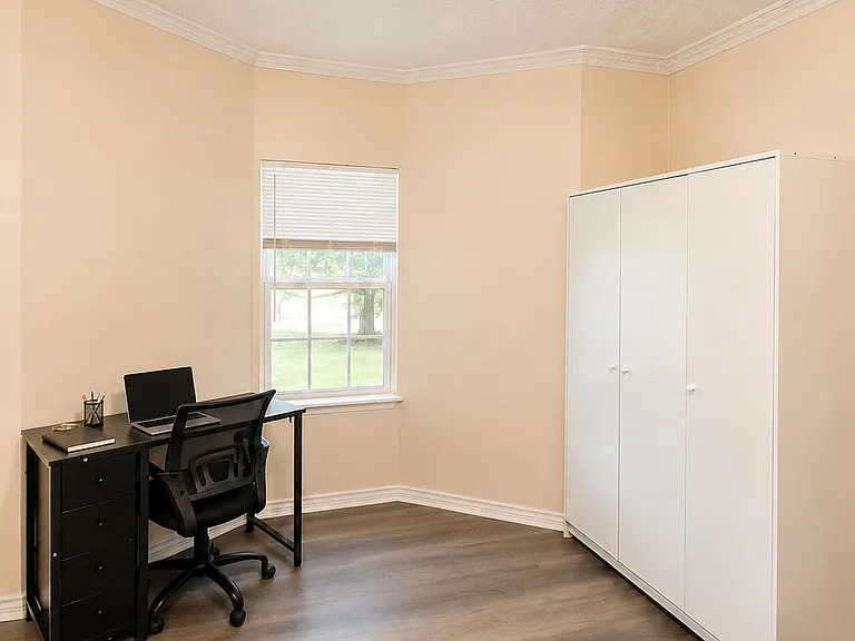 Well-sized bedroom with a window for natural light, durable flooring, a work desk, and a spacious wardrobe for storage.