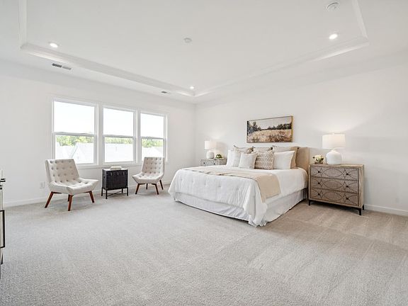 Tucked-away primary bedroom suite with seating area and tray ceiling