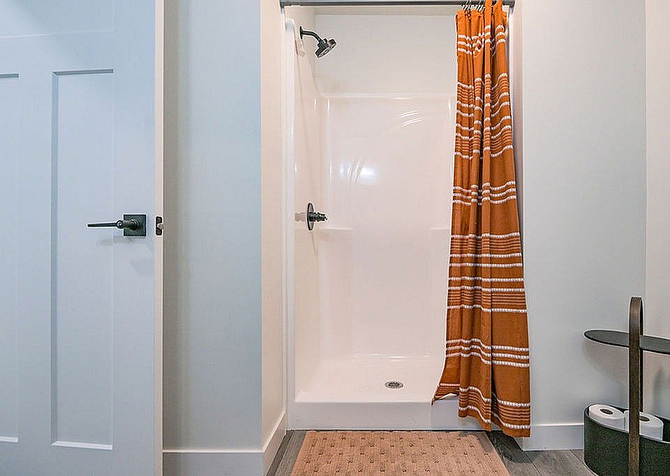 Modern bathroom featuring a sleek shower with an elegant orange stripe curtain, complemented by a stylish storage shelf and a contemporary door design.