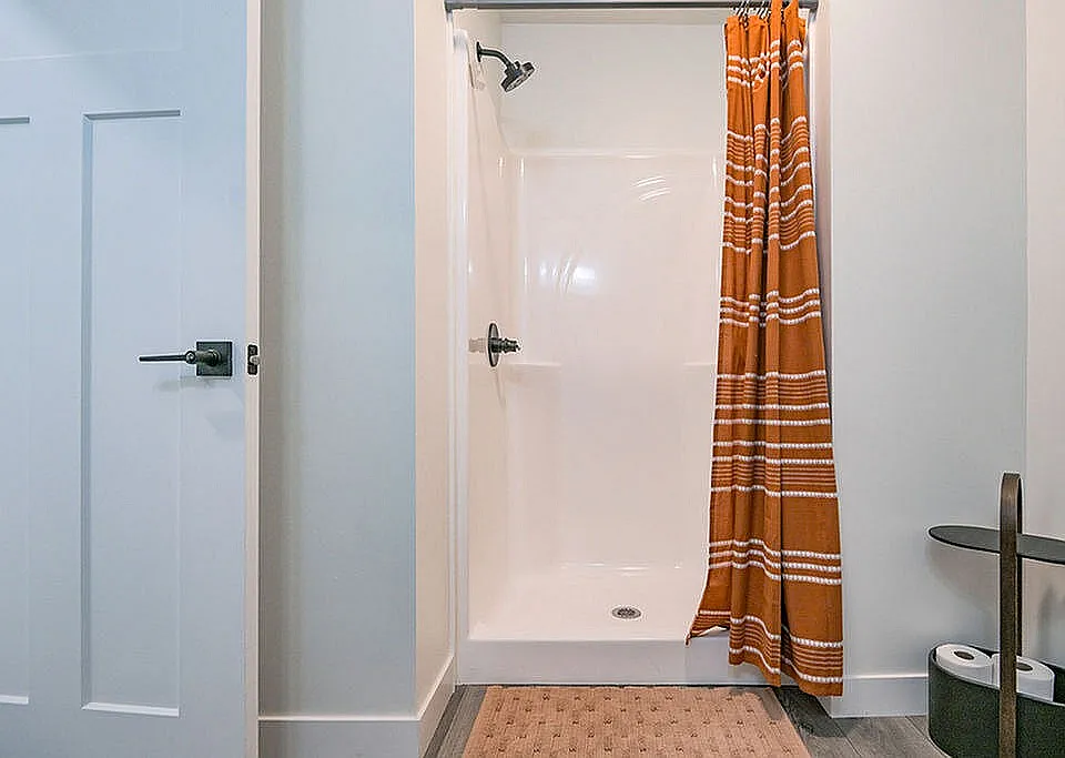 Modern bathroom featuring a sleek shower with an elegant orange stripe curtain, complemented by a stylish storage shelf and a contemporary door design.