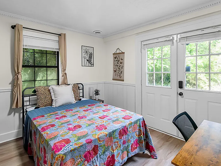 Bedroom 4 featuring a full-size bed & private entrance onto a concrete patio with a view of the woods