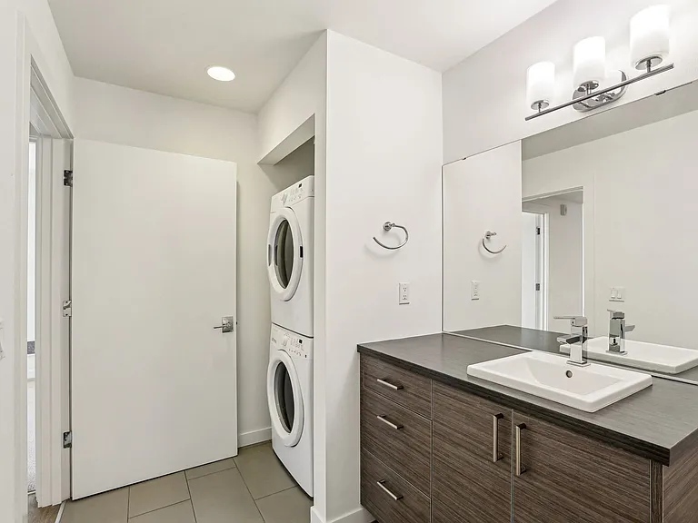 Modern bathroom with sleek vanity, white sink, and convenient in-unit stacked washer and dryer at 4400 Alaska in Seattle, WA. Enjoy contemporary amenities fo...