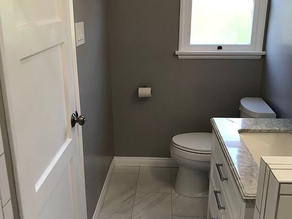 The adjacent bathroom is tiled with clean white and grey floor and shower. The sink has marble countertop.