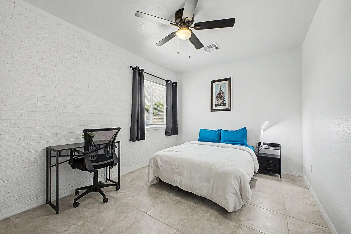 Private bedroom with a full bed, nightstand, and dedicated desk workspace, plus a window with curtains and ceiling fan. - N 42nd Ln
