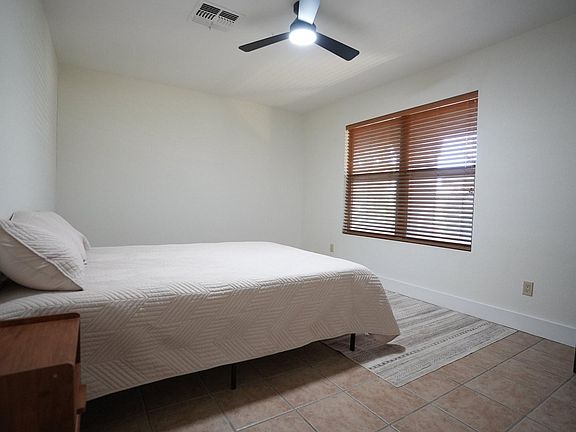 Private bedroom with a ceiling fan, large window with blinds, and space for a bed plus a desk/work area.