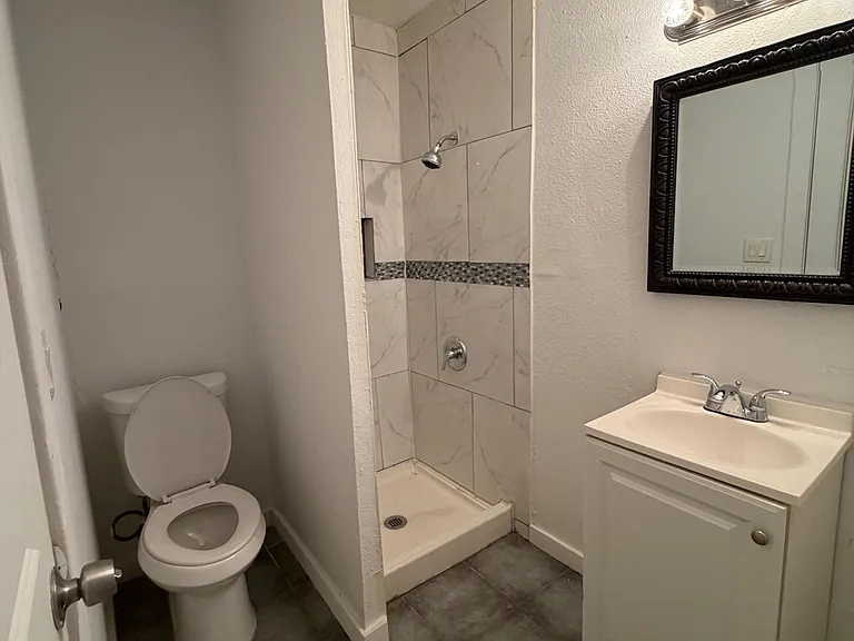 Full bathroom with tiled walk-in shower, vanity with mirror lighting, and durable tile flooring for easy upkeep.