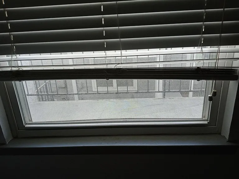 Window with blinds provides natural light and ventilation, offering a view to the exterior walkway.