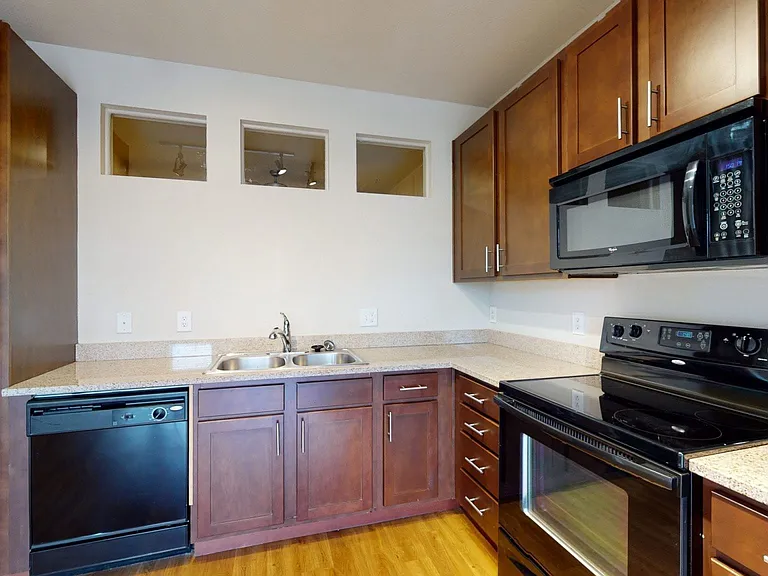 Apartment kitchen with granite countertops and wood-style flooring.