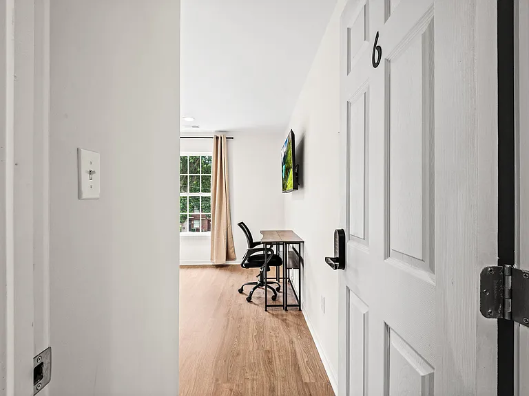 Private room with wood-look flooring, a work desk, and a wall-mounted TV, plus a window with curtains for natural light.