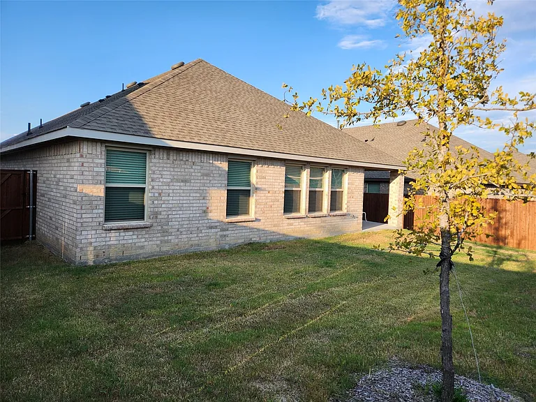 Rear exterior featuring light-colored brick siding, a brown asphalt shingle roof, and multiple windows with horizontal blinds