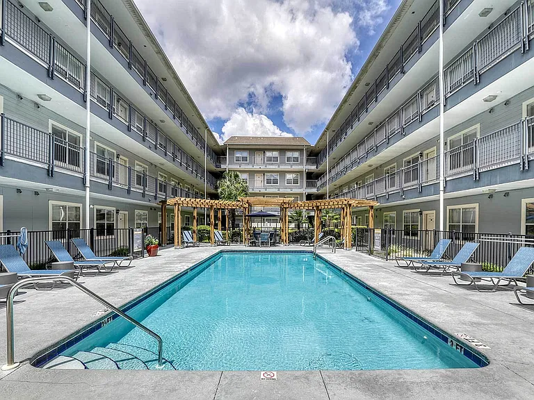 Inviting apartment complex showcasing a serene swimming pool surrounded by sleek lounge chairs, set against stylish multi-level balconies.