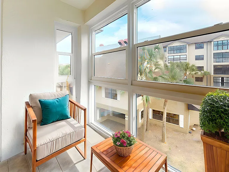 Charming sunlit nook featuring a comfortable armchair with a vibrant teal cushion, complemented by flourishing houseplants and expansive windows with a tranquil courtyard view.