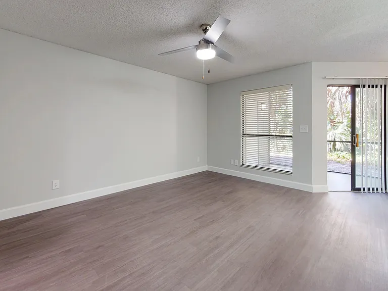 The Martinique floor plan offers a spacious living room filled with natural light, featuring modern flooring, a ceiling fan, and direct access to a private patio through sliding glass doors.