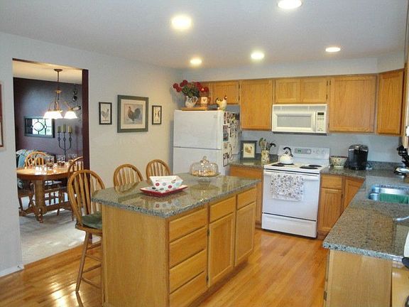 The island kitchen features granite counter tops, hardwood floors plus decorative glass door to pantry.