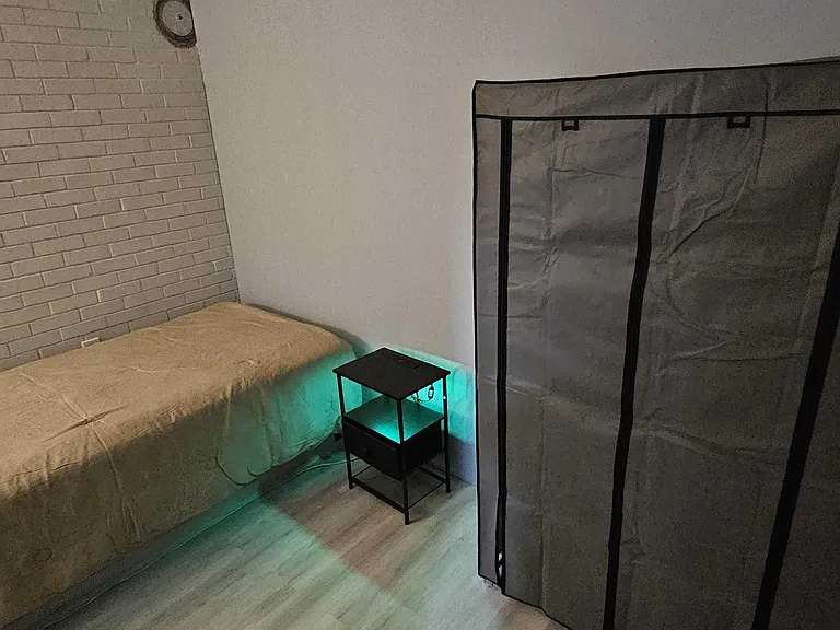 Private sleeping area with a twin bed, side table, and a freestanding wardrobe for everyday storage.