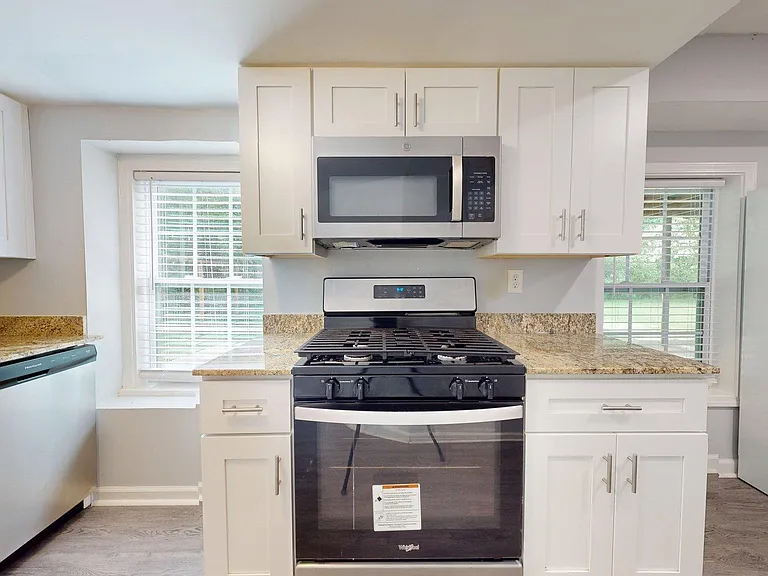 Updated kitchen with granite countertops, ample white cabinetry, and stainless steel appliances, plus window views.