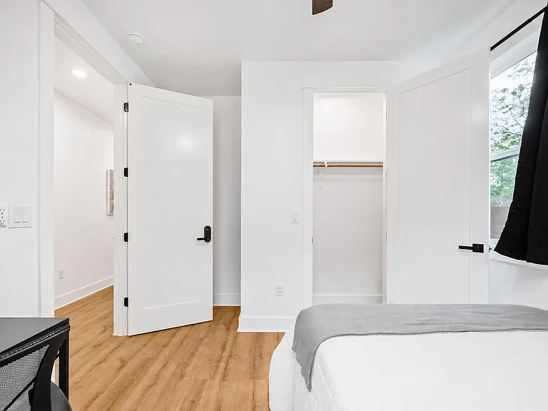Private bedroom with hardwood floors, an open closet with shelf and rod, and a large window for natural light.