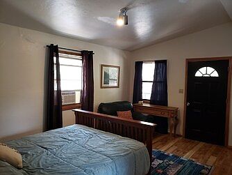Upstairs front bedroom, queen bed, sink with mirror, access from balcony with exterior stairs to parking level, walk-in closet, door into bathroom, hardwood floor, window a/c, ceiling fan with overhead light, baseboard heater.
