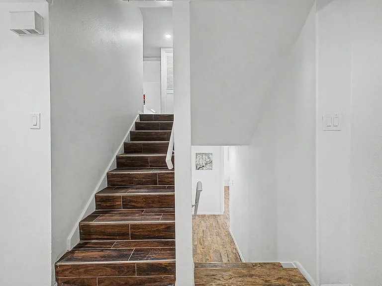 Split-level stairway with wood-look tile steps, clean white walls, and easy access between floors and hallway areas.