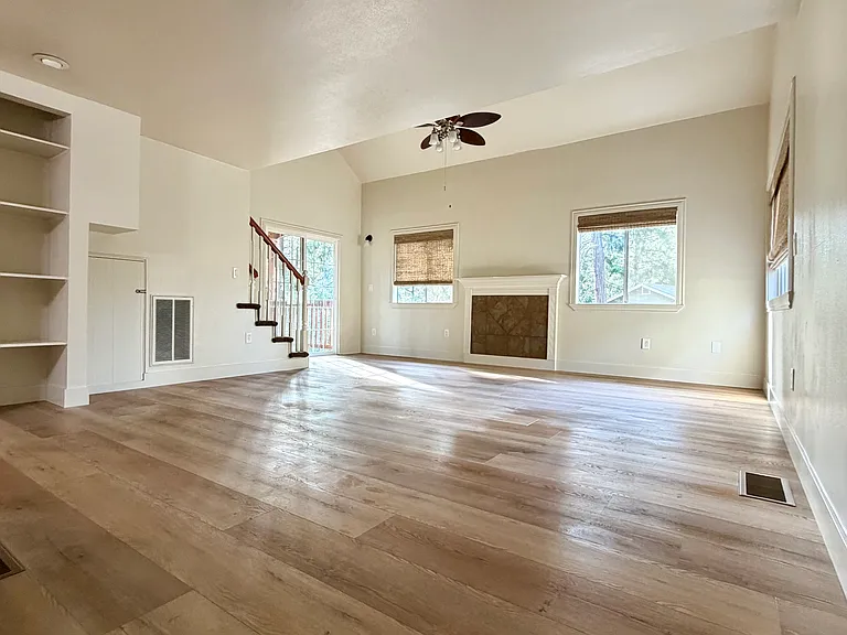 Well-lit dining and living area with ceiling fan, shelving, and sliding door out to deck