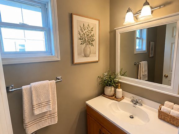 The first-floor half bath offers a convenient main-level location and features neutral tones, tile flooring, a spacious vanity, and a large mirror, making it both practical and appealing for everyday use.