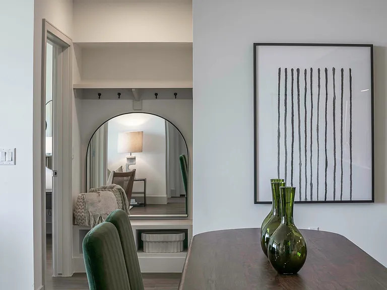Close-up view of a dining table with green vases, modern wall art, and a decorative mirror reflecting a cozy interior.