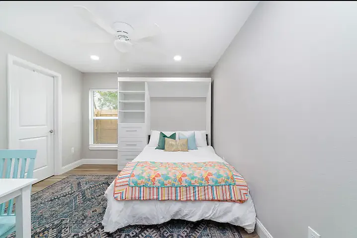 Full-sized murphy bed in downstairs bedroom with soft linens, fresh decor, and ample storage space. Workspace converts to a table for 4 during the day when bed is up.