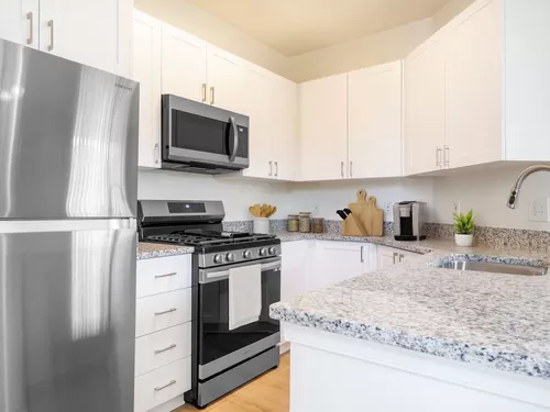 Renovated Package I kitchen with white cabinetry, grey granite countertops, stainless steel appliances, and hard surface plank flooring - Avalon Russett